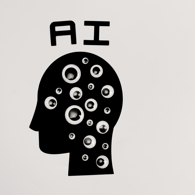 Cartoon silhouette of a human head with the letters AI above it. The head shape is covered in googly eyes